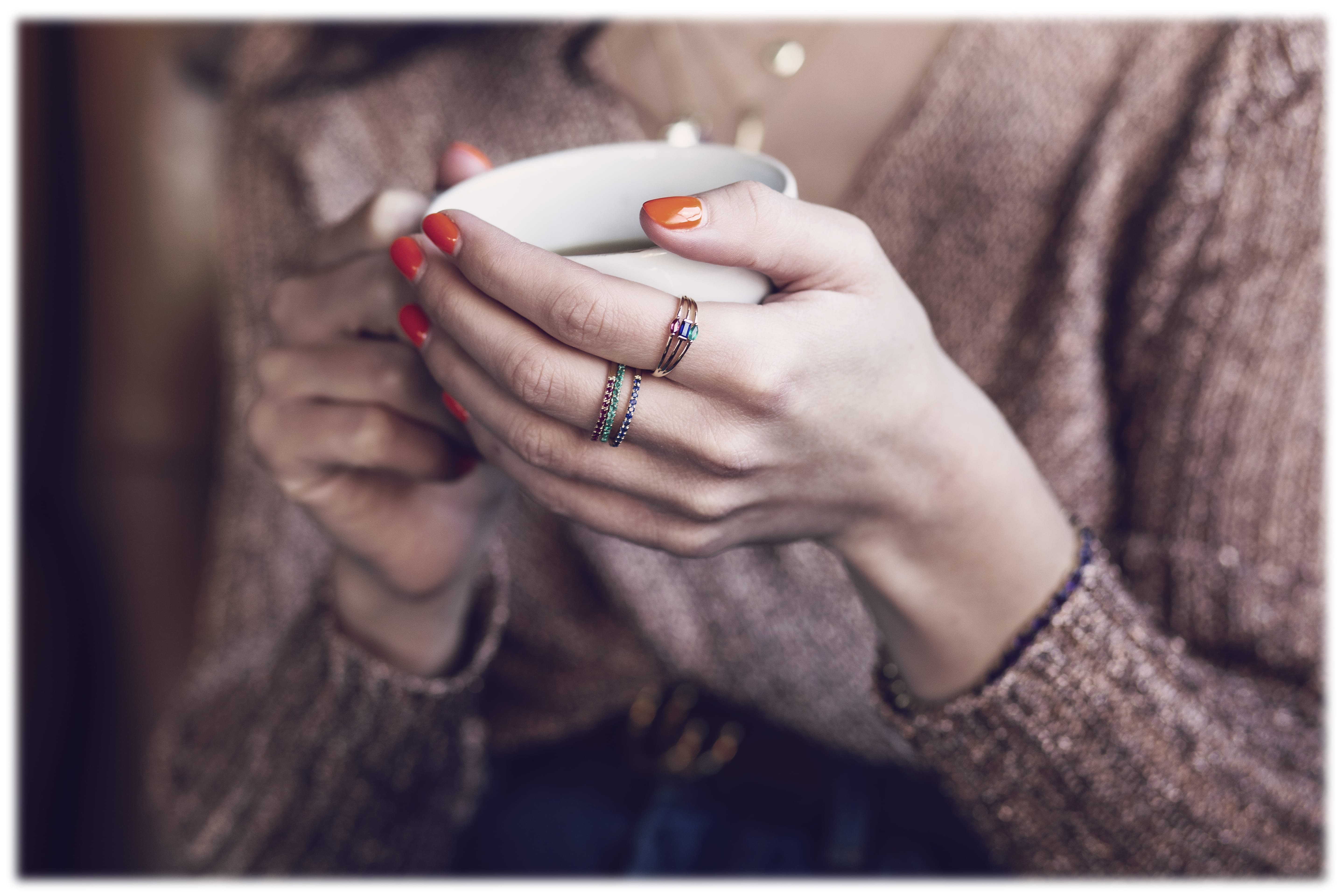 A woman holding a coffee cup is wearing 3 Joshua James gold & gemstone rings 