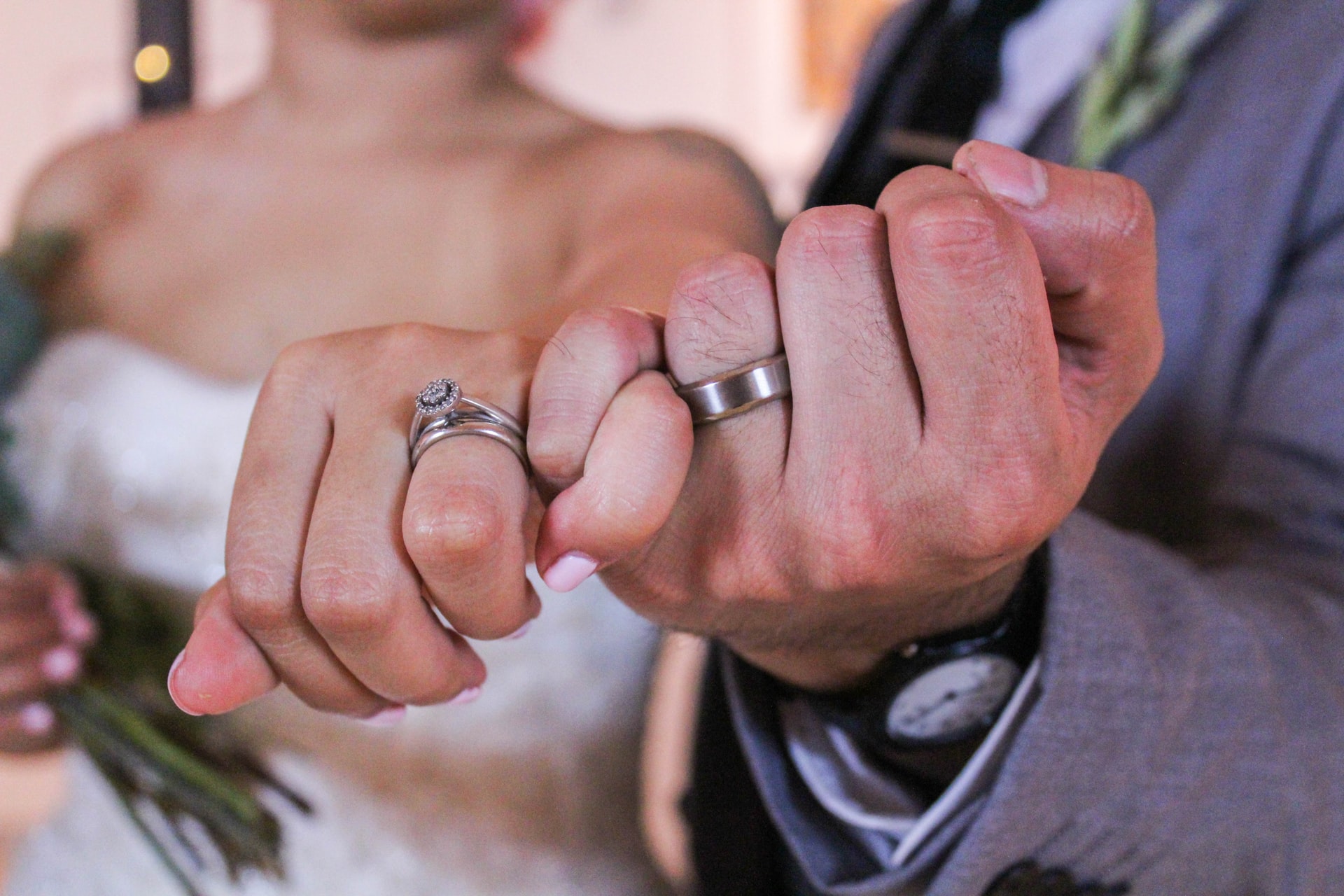 Close up of bride and groom making 'pinky promise' showing their wedding rings on fourth finger