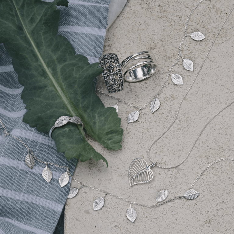 Ethical jewellery laid out by the brand Joshua James. Rings, necklaces and bracelets are placed over a marble floor, and wrapped around a leaf