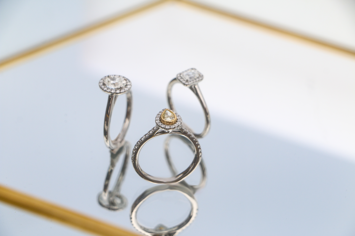 Image shows 3 different diamond engagement rings on a reflective surface.