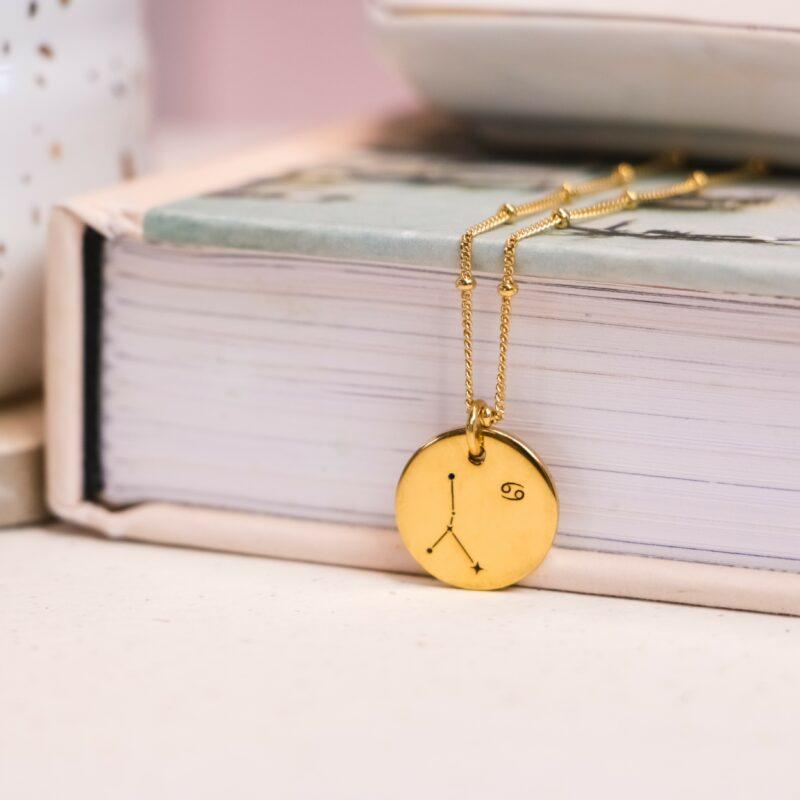 Christmas gifts for friends. A gold zodiac necklace on a pink backdrop.